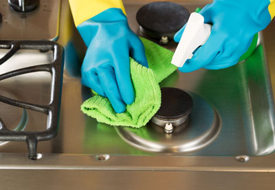 blue gloves, towel and spray cleaning stove top